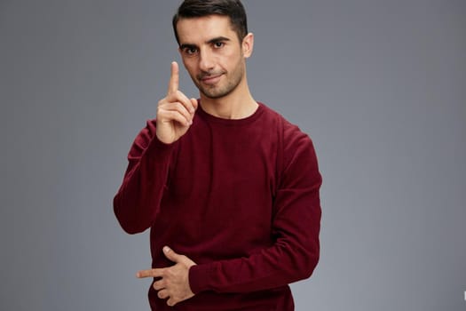 successful man holding index finger near face posing gesture with hands red sweater Gray background. High quality photo