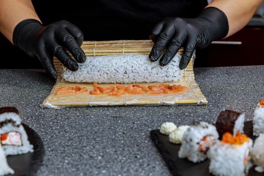 A female chef prepares Japanese sushi rolls. All sushi are made up of a base ingredient, specifically cooked rice, to which other ingredients are added.