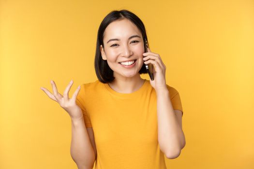 Young korean girl talking on mobile phone. Asian woman calling on smartphone, standing over yellow background.