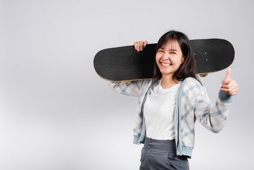 Smiling happy woman hold skateboard on shoulder and show thumb up good sign, Happy Asian beautiful young female excited hold hands longboard, studio shot isolated on white background with copy space