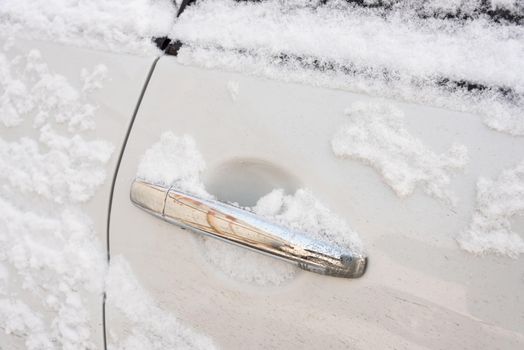 The door lock of car in the snow, close-up, in winter. The cars door handle is covered with snow.