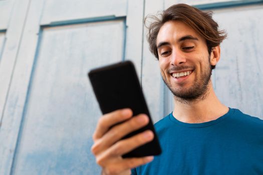 Close up portrait of smiling young caucasian man using mobile phone outdoors. Copy space. Selective focus on face. Lifestyle and social media concept.