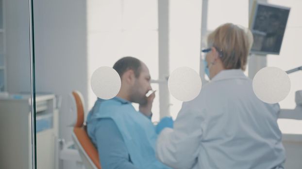 Mature dentist doing oral care consultation with patient in stomatology office. Dentistry expert talking to man about toothache and procedure to treat caries with stomatological tools.