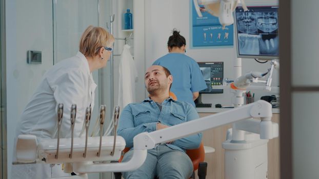 Patient attending consultation with senior dentist in dentistry cabinet. Stomatologist talking about oral care with man and doing dental checkup consultation, healthy denture examination.