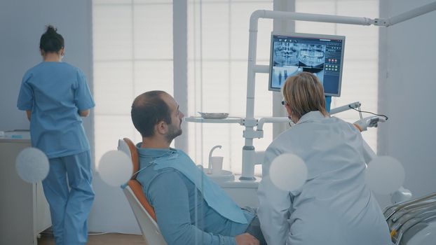 Specialist and patient looking at monitor with x ray scan to understand stomatological diagnosis at oral care clinic. Stomatologist and man analyzing radiography results on display.