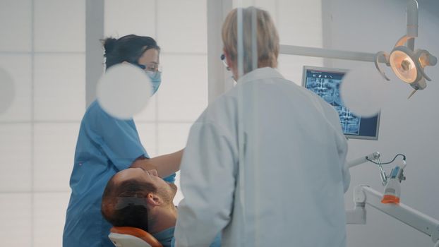 Stomatologist and nurse doing extraction procedure on patient to cure toothache. Dentistry team using dental tools and drill for stomatological surgery in cabinet. Orthodontic examination