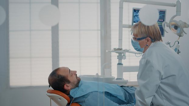 Stomatologist woman consulting patient after teeth procedure, analyzing denture with dental tools and instruments. Dentistry expert doing oral care examination in stomatological cabinet.