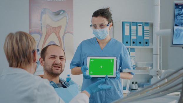 Nurse and patient analyzing green screen on digital tablet in dentistry cabinet. Dental assistant looking at blank chroma key with mock up template and isolated background on copy space gadget.