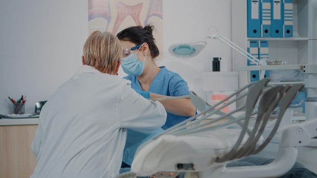 Team of specialists consulting patient with toothache, using drill instrument for dental procedure in dentistry cabinet. Stomatologist and assistant doing oral care examination.