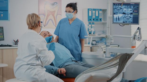 Dentist doing oral care examination on patient with toothache, using dental tools and instruments in stomatology office. Dentistry expert and nurse consulting teeth at appointment.