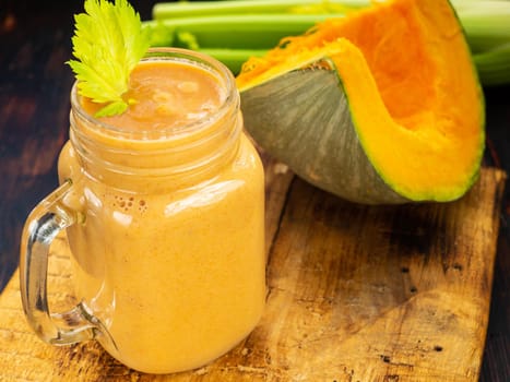 Pumpkin smoothie with celery leaves with a piece of pumpkin and celery stalks in the background.