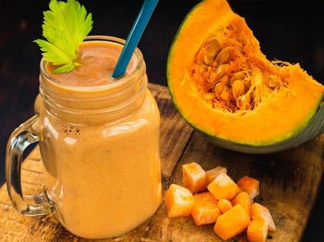 Pumpkin smoothies with celery leaves with a piece or pieces of pumpkin and a straw.