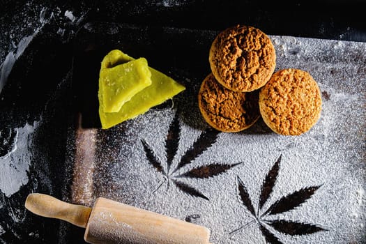 traces of marijuana leaves on flour, and rolling pin and three cookies and cannabis butter. on a rusty pan. top view flat lay. Horizontal orientation