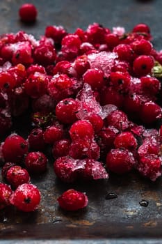 Frozen ice red currants pile lie on a rusty surface. dark. vertical orientation. close-up