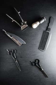 On a black dusty surface are old barber tools. Vintage manual hair clipper comb razor shaving brush shaving brush hairdressing scissors. black monochrome. vertical. top view. flat lay.