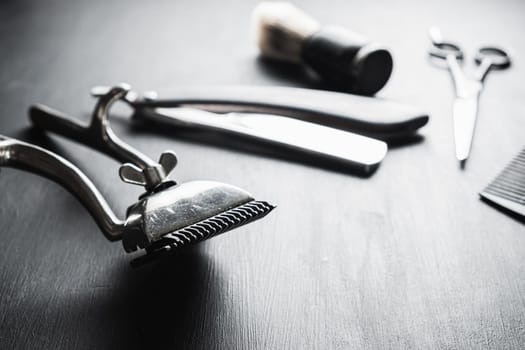 On a black dusty surface are old barber tools. Vintage manual hair clipper comb razor shaving brush shaving brush hairdressing scissors. black monochrome. horizontal.