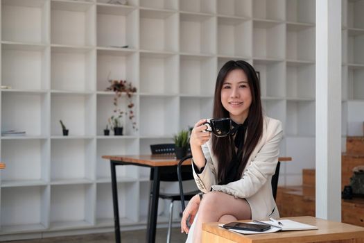 Portrait attractive asian businesswoman smiling and look at camera while working on laptop at modern office