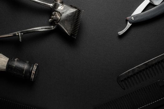 On a black surface are old hairdresser tools. vintage hand-held hair clipper, hairdressing scissors, combs, razor, shaving brush. black monochrome. horizontal orientation. top view flat ley