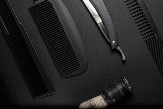 On a black surface are old hairdresser tools. combs, razor, shaving brush. black monochrome. horizontal orientation. top view flat ley.