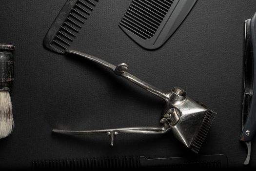 On a black surface are old hairdresser tools. vintage hand-held hair clipper, hairdressing scissors, combs, razor, shaving brush. black monochrome. horizontal orientation. top view flat ley