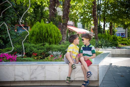 Group of happy children playing outdoors. Kids having fun in park during summer vacation. Friends sitting in sunglasses and smiling. Summer holiday concept.