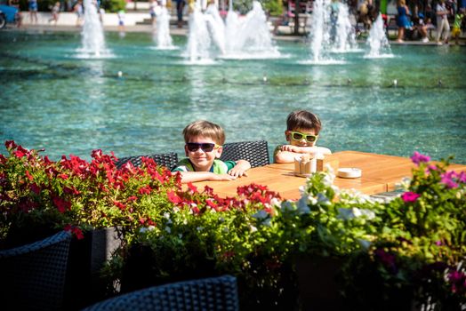 Two little kid boys waiting on table for healthy breakfast in hotel restaurant or city cafe. Summer holiday with children concept.