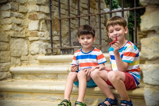 The children playing on the ruins of ancient building with metal gate an archaeological site of an ancient city. Two boys sitting and play with toy aircraft plane. Travel concept.