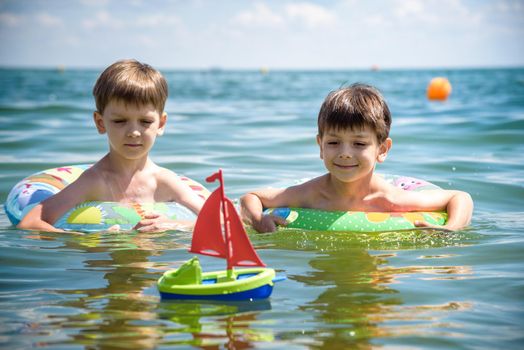 Happy kids have fun in sea surf on beach. Joyful couple of children on inflatable ring ride on breaking wave. Travel lifestyle, swimming activities in family summer camp. Vacations on tropical island.