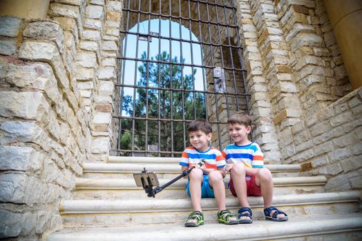 Two cute little brothers sitting on stairs in Italian town. Make selfie on mobile phone. Kids smiling and happy having leisure time on summer holiday.