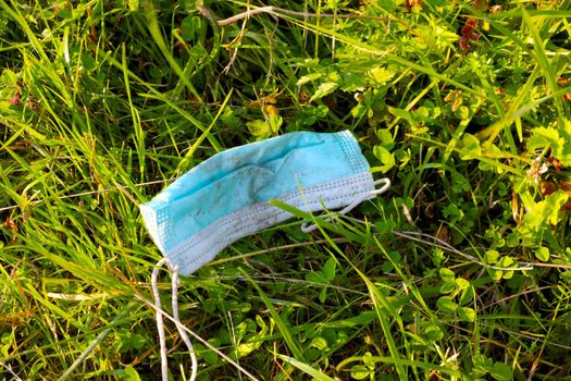 A dirty used medical mask lies in the grass