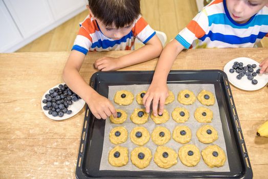 happy family funny kids are preparing the dough, bake cookies in the kitchen. Put berry and blueberry in all biscuits.