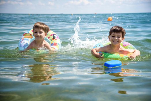 Happy kids have fun in sea surf on beach. Joyful couple of children on inflatable ring ride on breaking wave. Travel lifestyle, swimming activities in family summer camp. Vacations on tropical island.