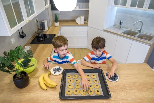 happy family funny kids are preparing the dough, bake cookies in the kitchen. Put berry and blueberry in all biscuits.