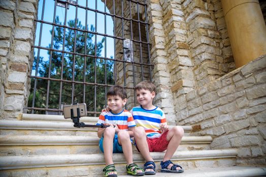 Two cute little brothers sitting on stairs in Italian town. Make selfie on mobile phone. Kids smiling and happy having leisure time on summer holiday.