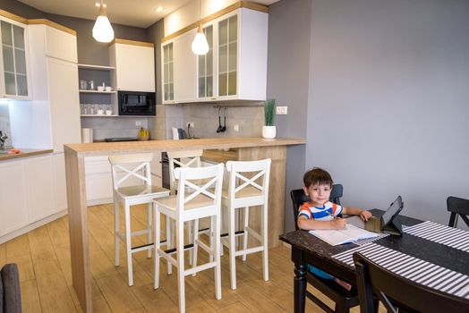 Smart preteen schoolboy doing his homework with digital tablet at home. Child using gadgets on his kitchen to study. Modern education and learning for kids.