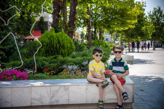 Group of happy children playing outdoors. Kids having fun in park during summer vacation. Friends sitting in sunglasses and smiling. Summer holiday concept.