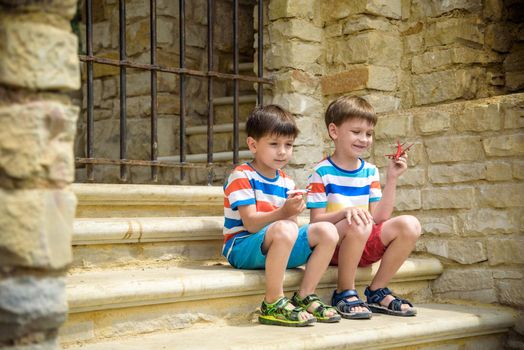 The children playing on the ruins of ancient building with metal gate an archaeological site of an ancient city. Two boys sitting and play with toy aircraft plane. Travel concept.