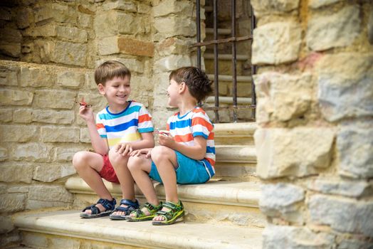 The children playing on the ruins of ancient building with metal gate an archaeological site of an ancient city. Two boys sitting and play with toy aircraft plane. Travel concept.