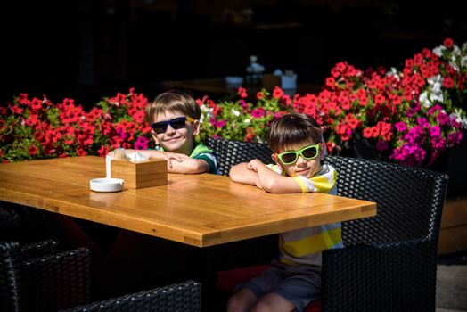 Two little kid boys waiting on table for healthy breakfast in hotel restaurant or city cafe. Summer holiday with children concept.