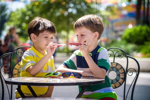 Two little kid boys waiting on table for healthy breakfast in hotel restaurant or city cafe. Child sit on comfortable chair play with toy aircraft, relaxed, enjoy their vacation. Summer holiday with children concept.