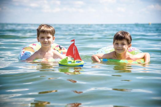 Happy kids have fun in sea surf on beach. Joyful couple of children on inflatable ring ride on breaking wave. Travel lifestyle, swimming activities in family summer camp. Vacations on tropical island.