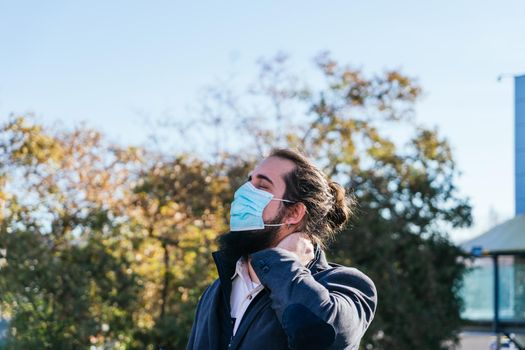 Young businessman with neck pain from work. He massages his neck near his offices on the street. Young entrepreneur with long hair and beard, brown, on a sunny day.