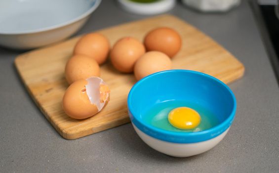 egg yolk in a blue bowl presentation. are some eggs in a wood table and salt and oil on the background