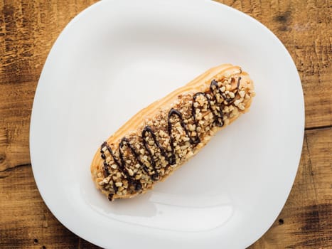 eclair on a white plate on wooden background. top view