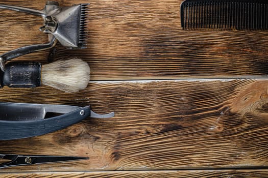 old hand hairdressing tools. Manual clipper, hairdressing scissors, straight razor, brush for shaving foam. on brown weathered wood background. top view flat lay. Horizontal orientation. copy space.