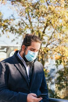 Young businessman with long hair and beard looking smartphone during his work break, on the street next to the offices. Vertical photo on a sunny and clear day.