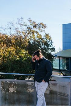 young businessman with long hair and beard, brown, laments because he receives bad news from his smartphone. He is outside near his offices during his work break.