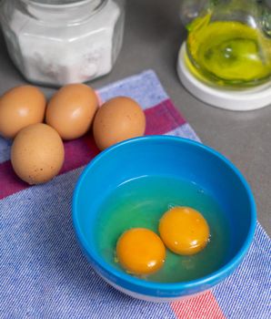 presentation of ingredients for culinary recipe, oil, salt and egg yolks in blue bowl They're prepared to cook in a home kitchen, placed up on a blue cloth in a gray countertop. Salt are into a glass pot and egg yolks are in a blue bowl.
