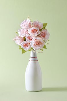 Bouquet of fresh pink flowers in a stylish unlabelled white champagne bottle over green with copy space for Valentines Day