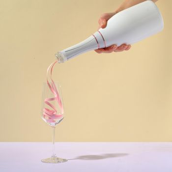 Hand pouring luxury rose champagne into an elegant flute over a beige background with copy space